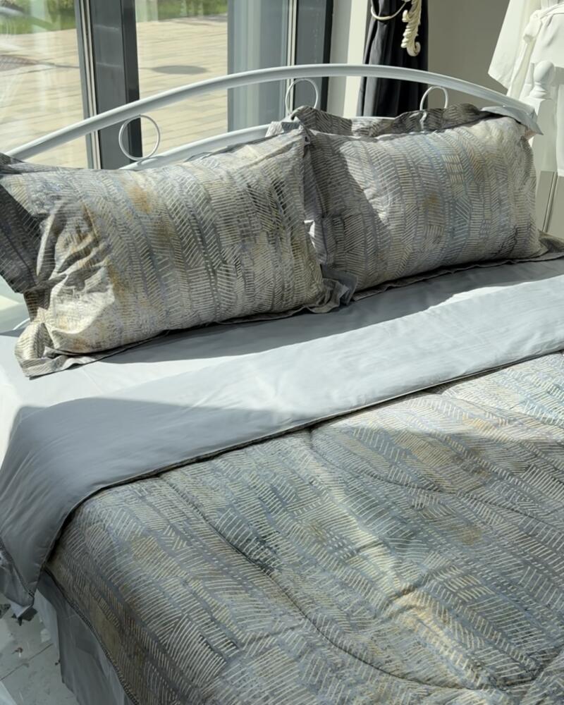 Close-up of a bed with patterned pillows and comforter in shades of gray and gold, featuring a white metal bed frame.