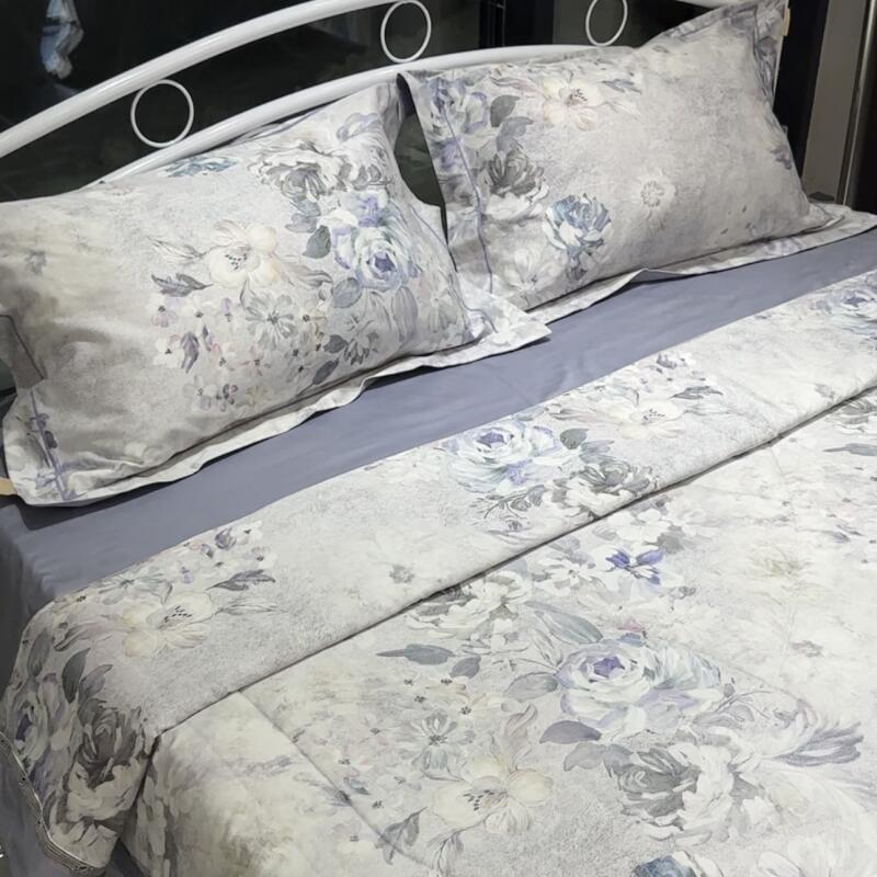 A bed is neatly made with a gray sheet, a floral patterned comforter, and two matching pillows, all under a white metal frame.