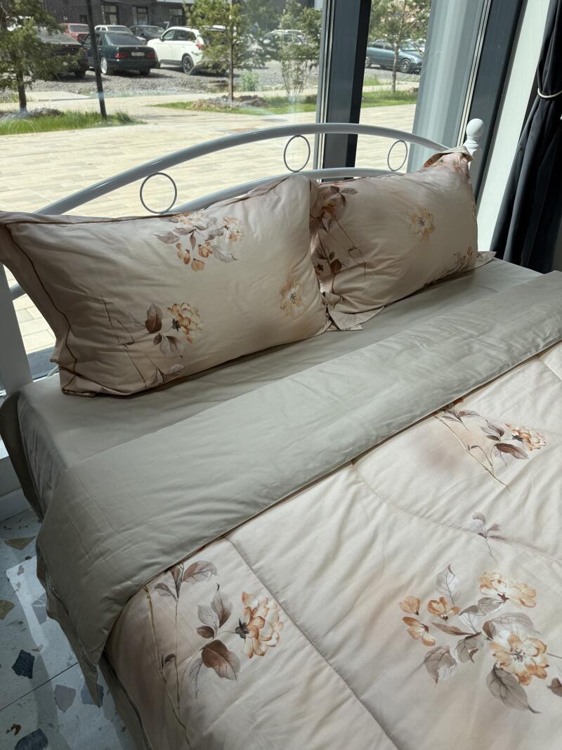 A bed with a white metal frame is neatly made with beige bedding featuring a floral pattern.