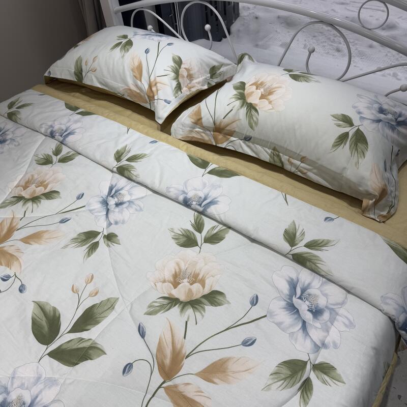 The photo shows a bed with floral-patterned bedding, including two pillows and a comforter, all featuring a light blue background with white and brown floral designs.