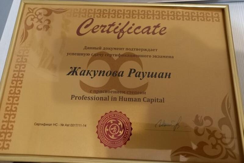 A framed certificate with gold trim reads 'Certificate,' followed by text in Russian stating that the document confirms the successful completion of a certification exam by Zhakupova Raushan, with the degree of 'Professional in Human Capital.'