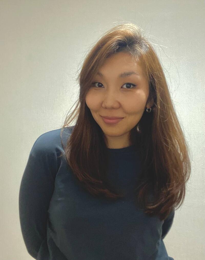 A woman with long brown hair is wearing a dark blue shirt and hoop earrings.