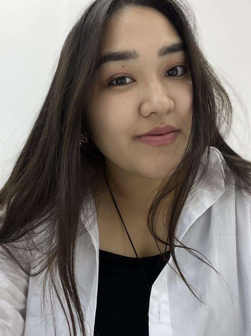 A young woman with long dark hair is wearing a white shirt over a black top.