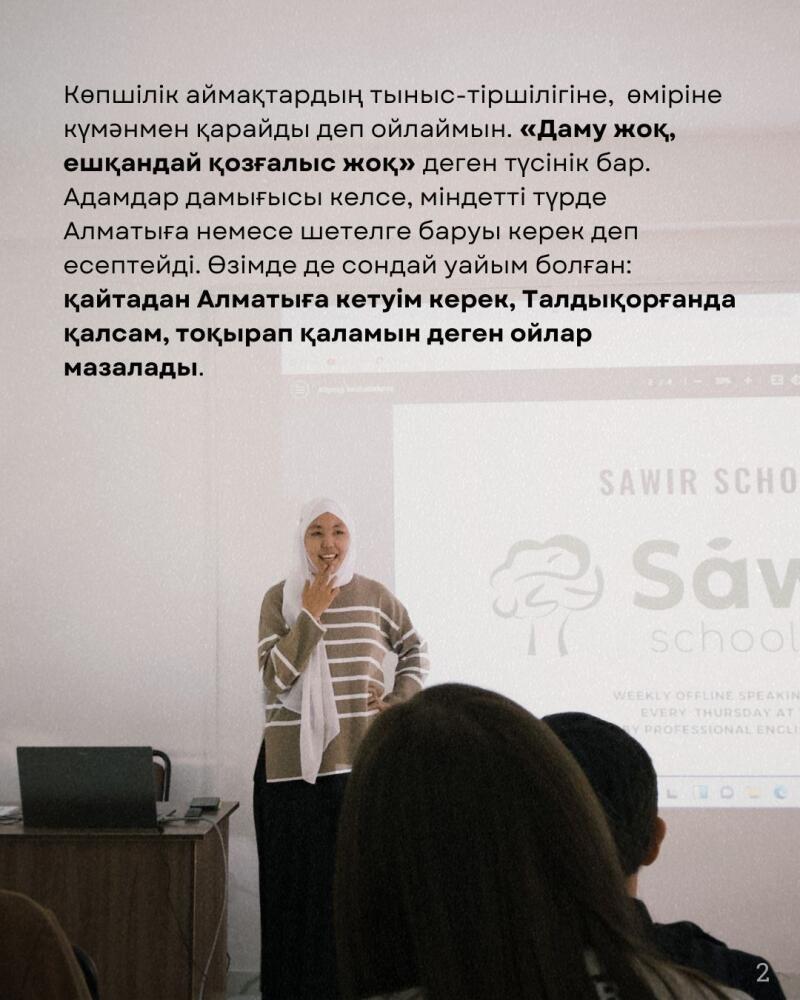 A woman wearing a hijab and a striped sweater is giving a presentation in front of an audience, next to a screen displaying the text "SAWIR SCHOOL."