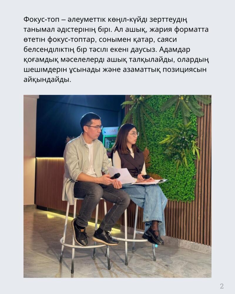 Two people are sitting on high chairs holding papers in their hands; the backdrop features a wall with green plants and wooden slats. Text is visible at the top.