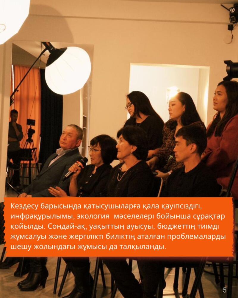 A group of people is seated in a row, with some holding microphones, under studio lighting; a text overlay in Kazakh discusses city safety, infrastructure, ecology, budget efficiency, and local government efforts to solve problems.