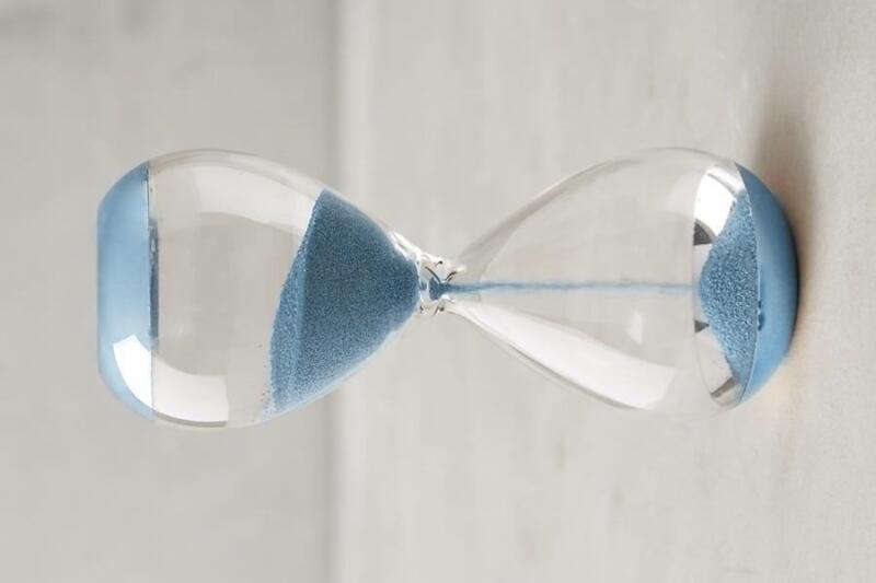 A blue sand hourglass is positioned horizontally, with blue sand mostly collected in the left bulb.