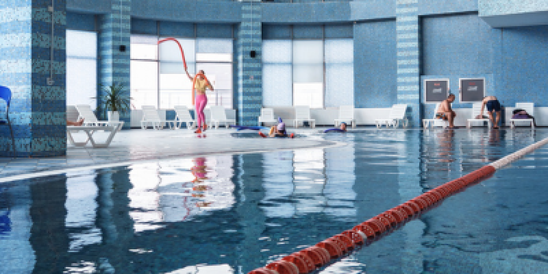 The image shows an indoor pool with several people: a woman is exercising with a rope, some are in the water, and two men are sitting on lounge chairs next to the pool.