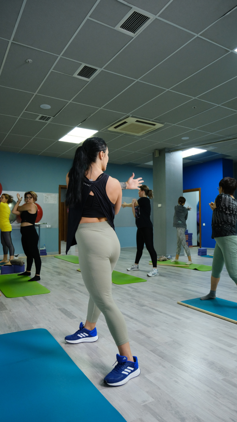 A group of women are doing stretching exercises on yoga mats in a room with a tiled floor and ceiling.