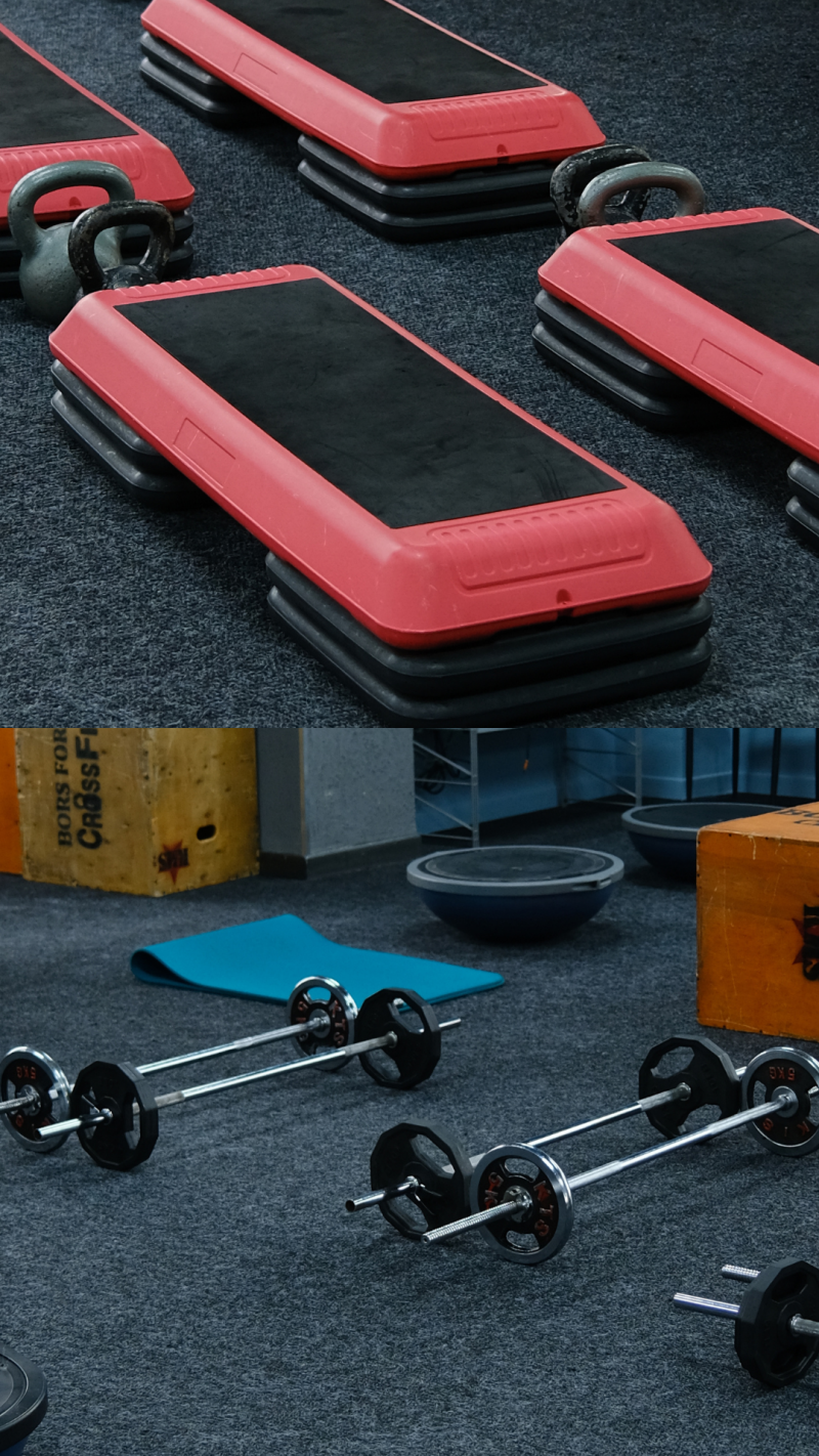 The image shows a fitness studio with equipment, including step platforms with red tops and black bases, kettlebells, barbells, balance balls, and a blue yoga mat.