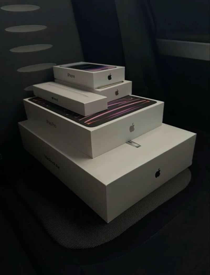 A stack of Apple product boxes, including iPhone, Pencil, iPad Pro, and Macbook Air, sits on a dark surface.