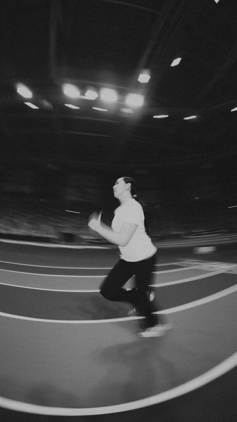 A woman in a t-shirt and pants runs on a track in a blurry, black-and-white photo.