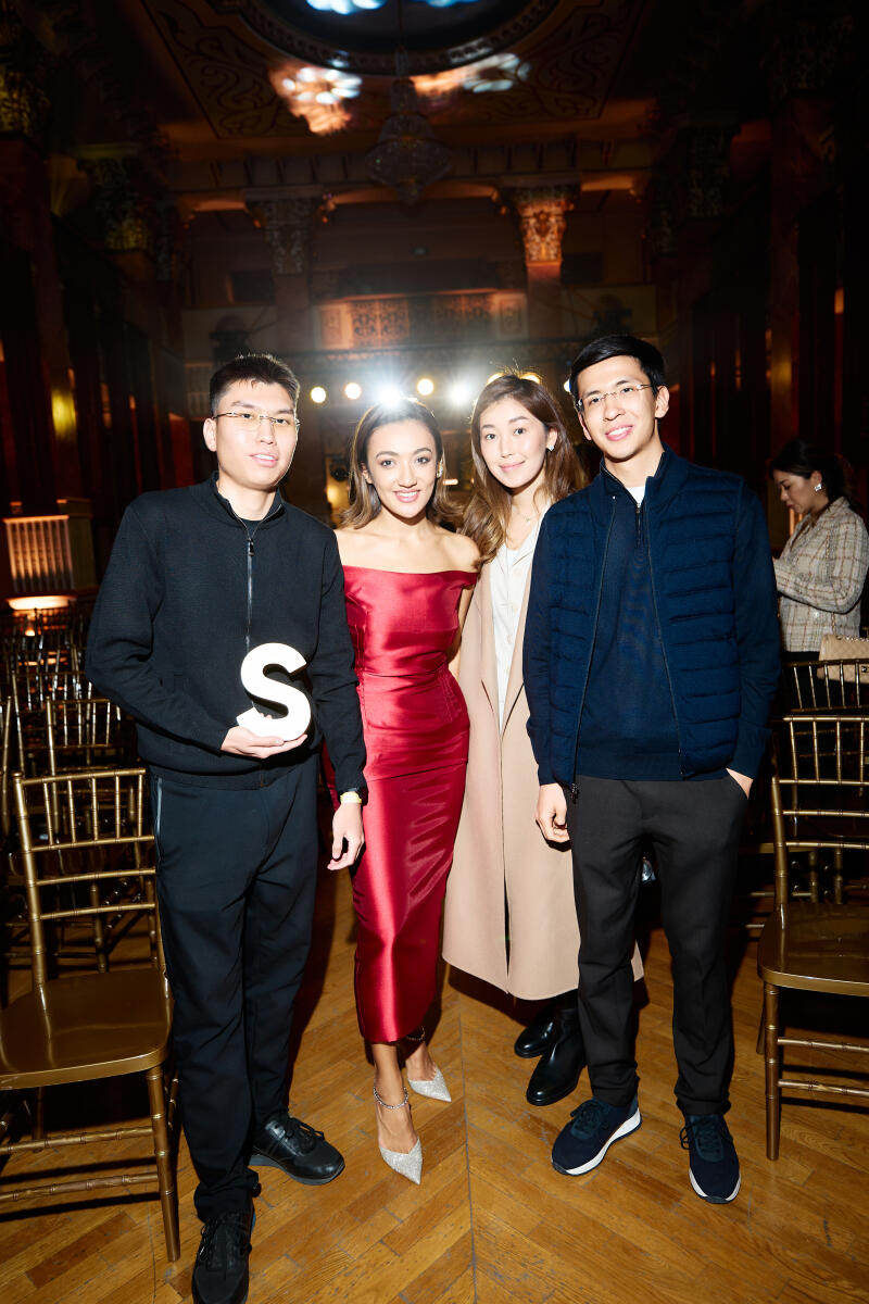 Four people are standing in a room; one of them is holding the letter "S."