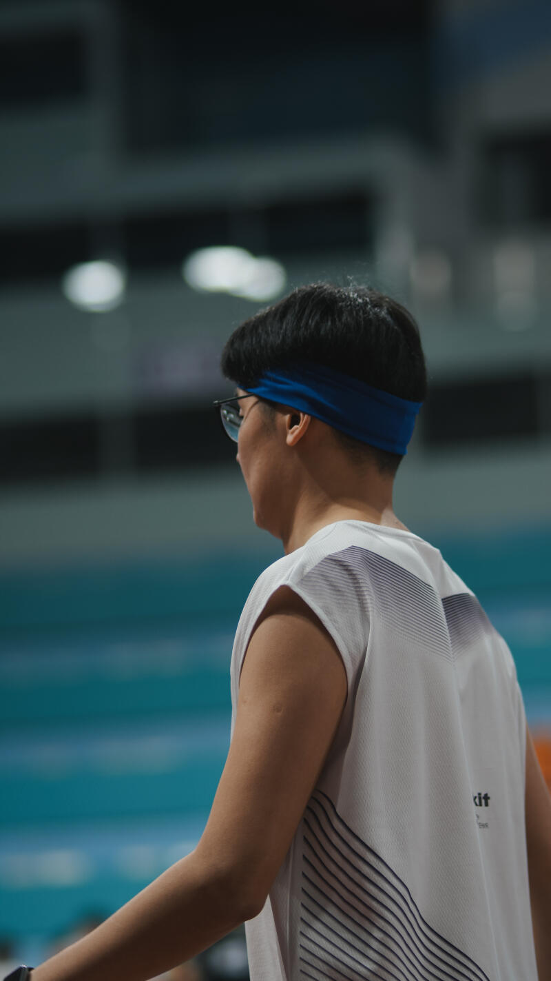 A person wearing glasses and a blue headband, seen from behind, with a white sleeveless shirt that has thin, dark stripes on the lower back.