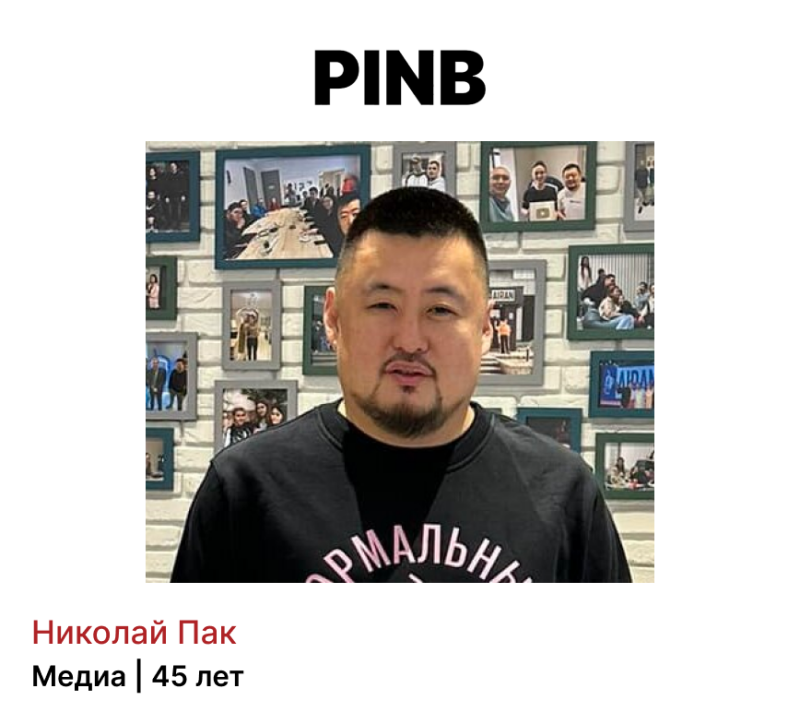 A portrait of Nikolai Pak, age 45, in front of a wall with framed photos, with the word "PINB" above him.