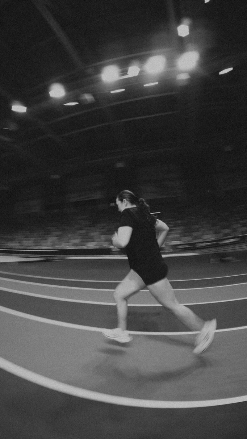 A woman in athletic wear is running on an indoor track in a black and white photo.