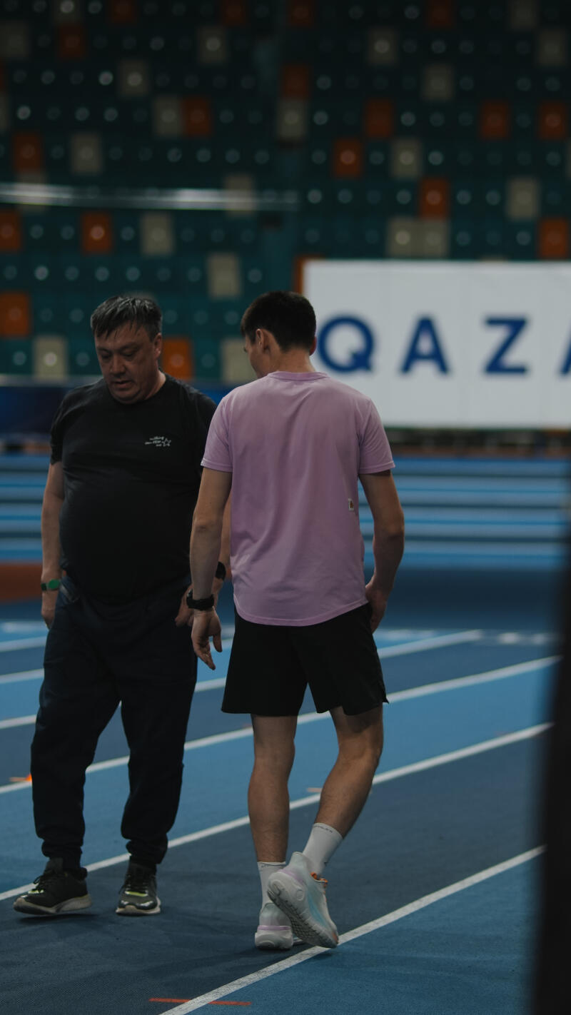 Two men are standing on a blue track, with the word "QAZ" visible in the background.