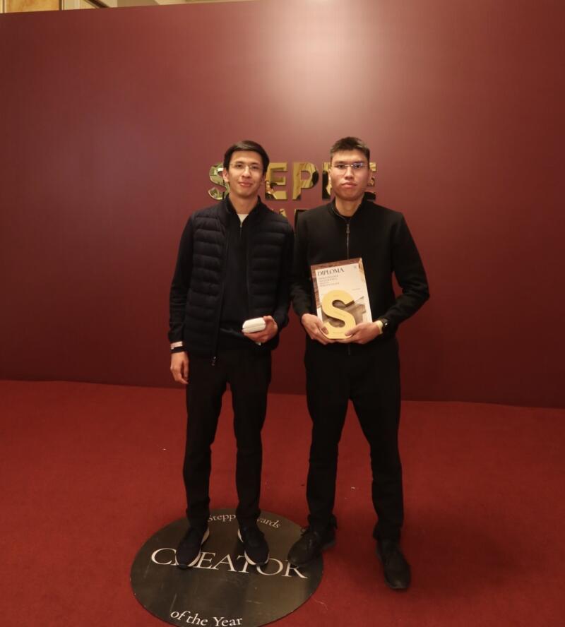 Two men in black attire stand on a round platform that reads "Creator of the Year", one holding a diploma with a prominent "S" design.