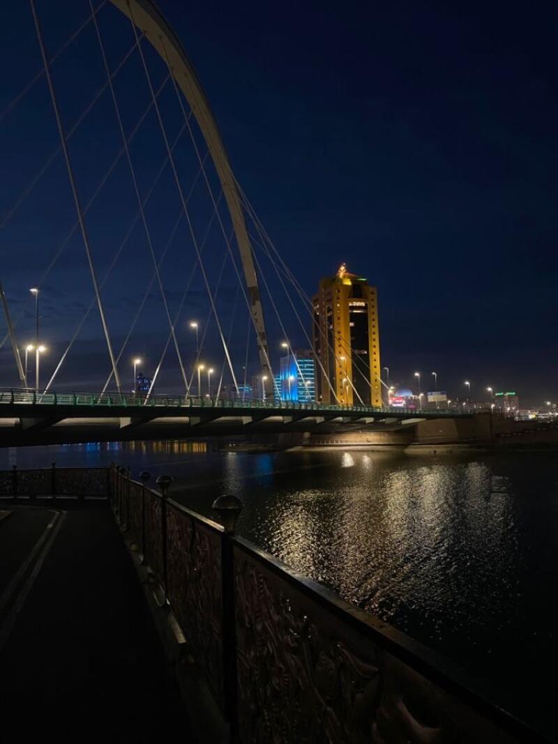 The night scene features a bridge illuminated with street lights, spanning over a river, with a tall golden building in the background.