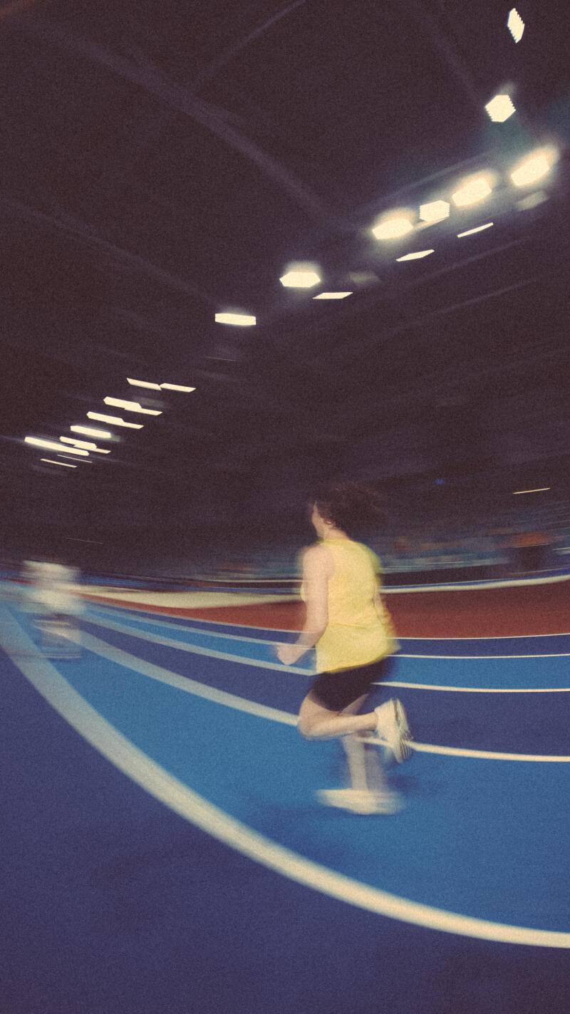 A blurry image shows a person running on a blue and red track under bright lights.