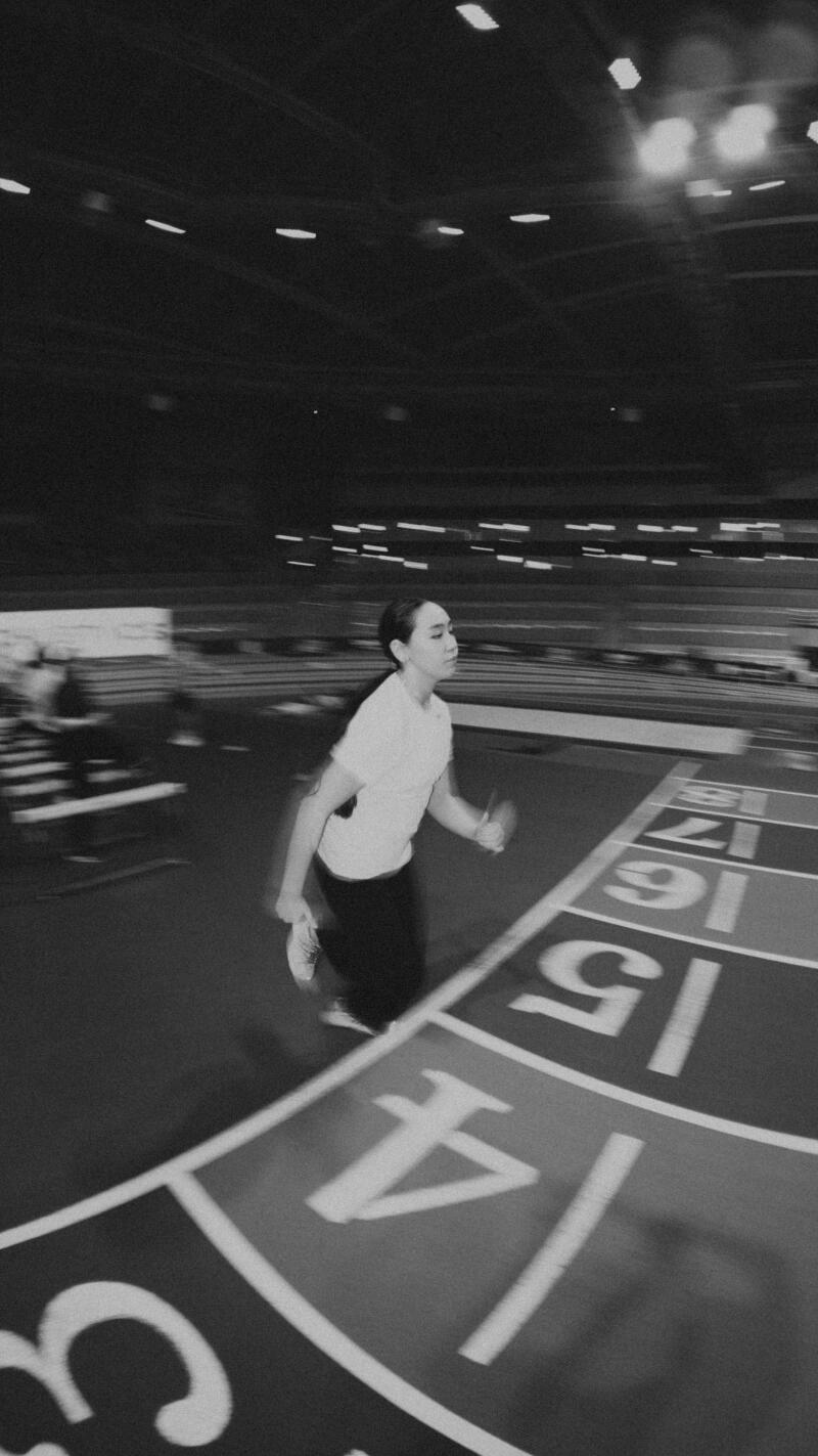A black and white shot shows a person running on an indoor track with lane numbers 3 through 6 visible.