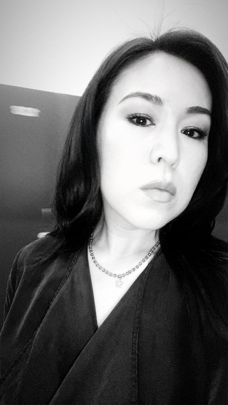 A grayscale close-up shot of a woman with dark hair wearing a necklace with a flower pendant.