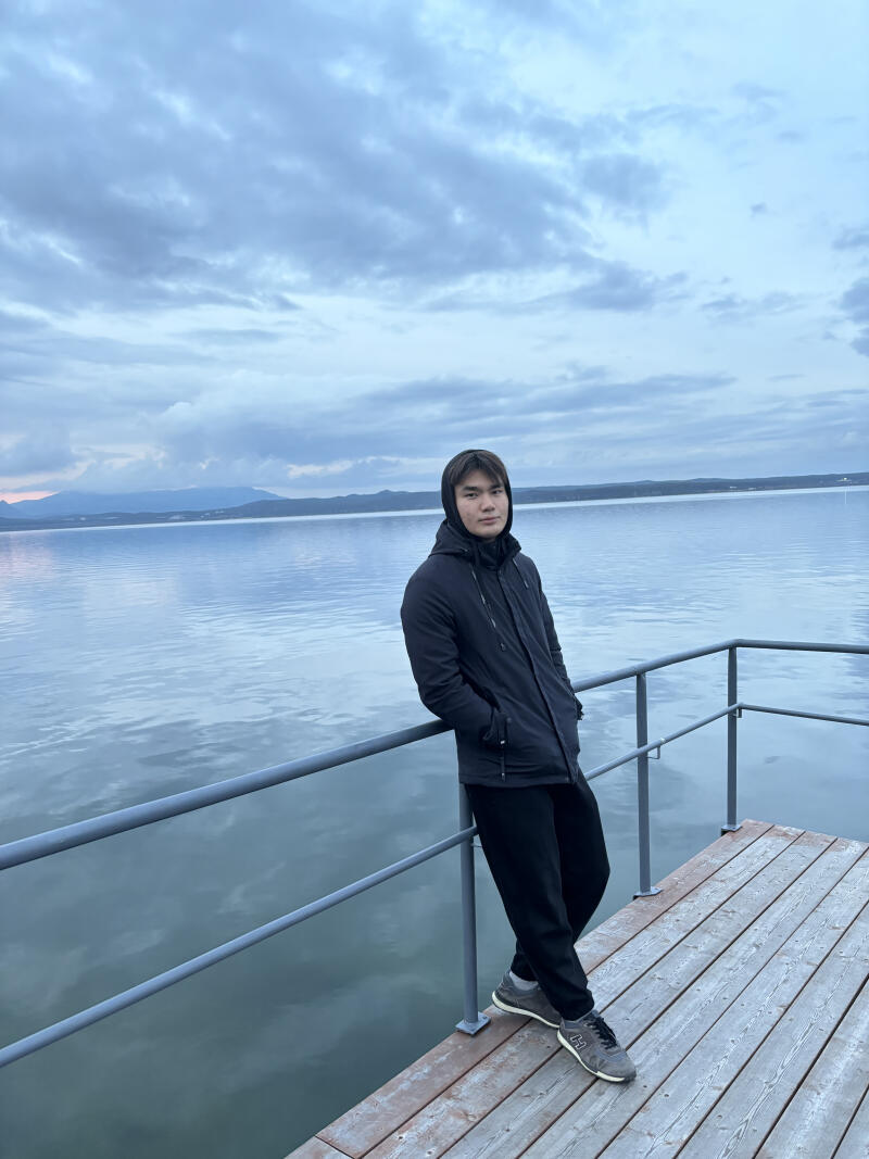 A man in a dark jacket is standing on a wooden pier by the water.