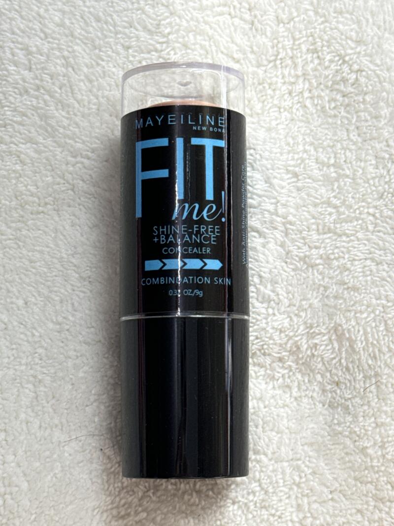 A Maybelline Fit Me! Shine-Free + Balance Concealer stick for combination skin is standing on a white textured surface.