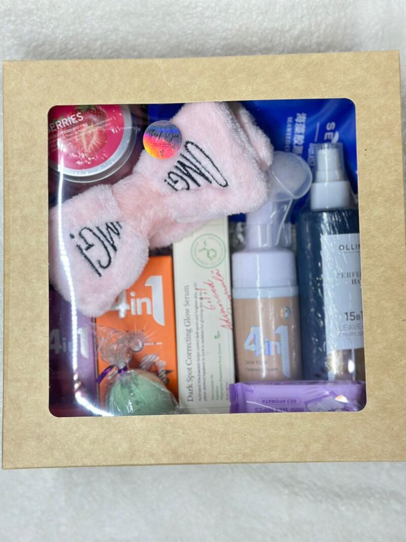 A box containing several beauty products, including a strawberry-scented item labeled 'BERRIES', a pink headband with 'OMG!', a 'Dark Spot Correcting Glow Serum', '4 in 1' cleanser, 'OLLIN Perfect Hair' leave-in cream, and other items.