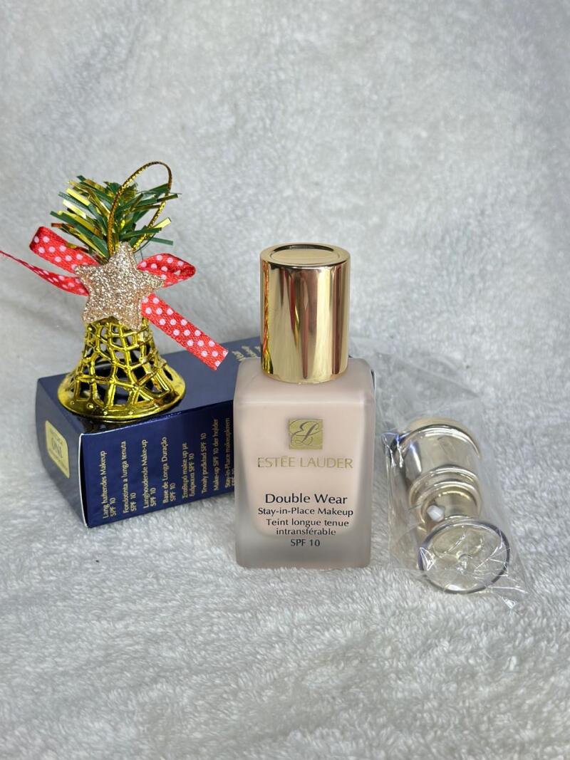 The image shows a bottle of Estee Lauder Double Wear Stay-in-Place Makeup SPF 10 next to its box and a Christmas bell decoration.
