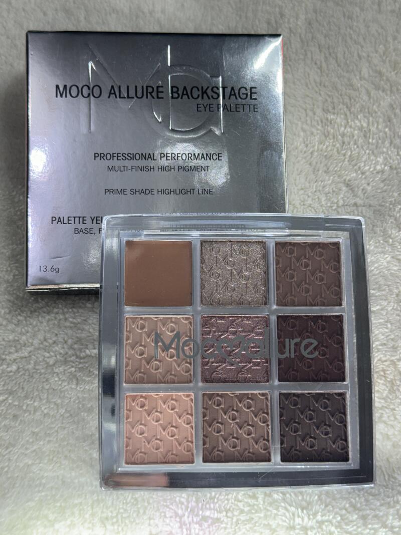 The image shows a "MOCO ALLURE BACKSTAGE EYE PALETTE" with nine eyeshadow colors in a clear plastic case, along with its silver box, which features the text "PROFESSIONAL PERFORMANCE MULTI-FINISH HIGH PIGMENT" and "PRIME SHADE HIGHLIGHT LINE".