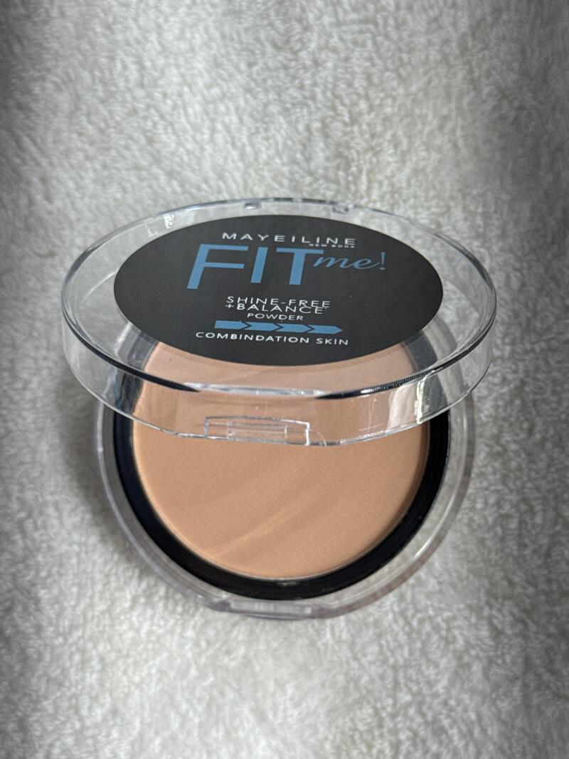 An opened container of Maybelline Fit Me! powder is displayed, showing the powder and the product label.