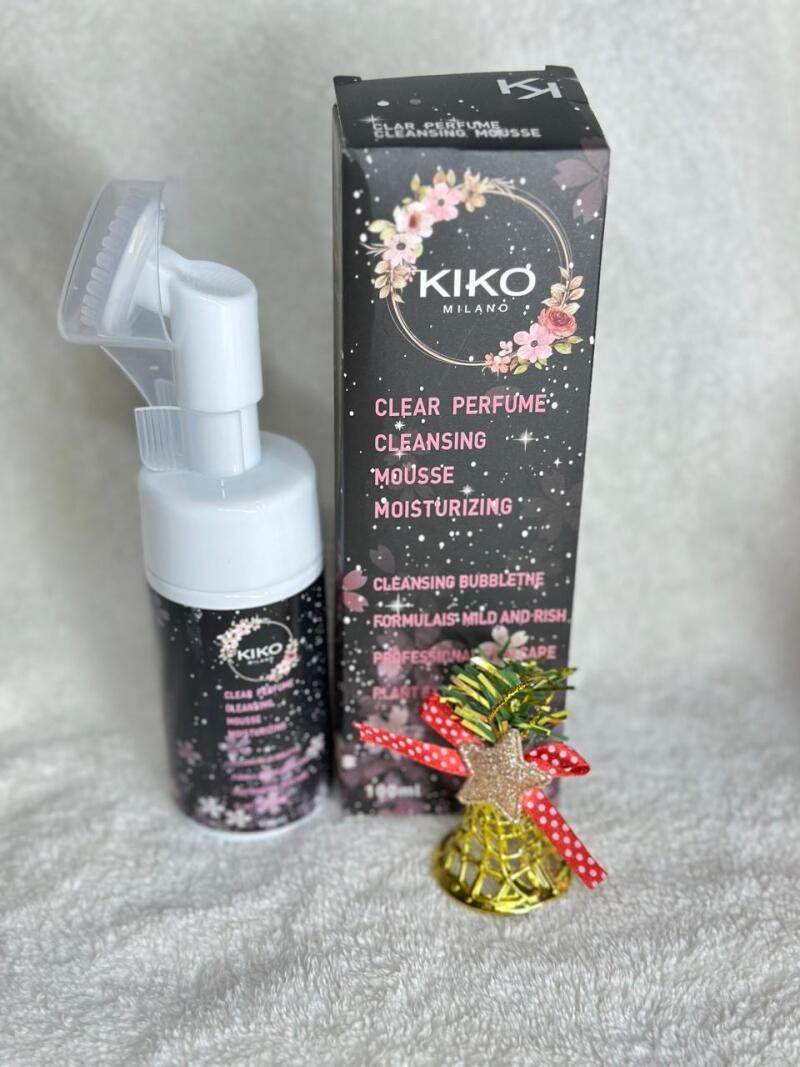 The image shows a Kiko Milano Clear Perfume Cleansing Mousse bottle with a pump and its packaging box, alongside a decorative golden bell with a star and ribbon.
