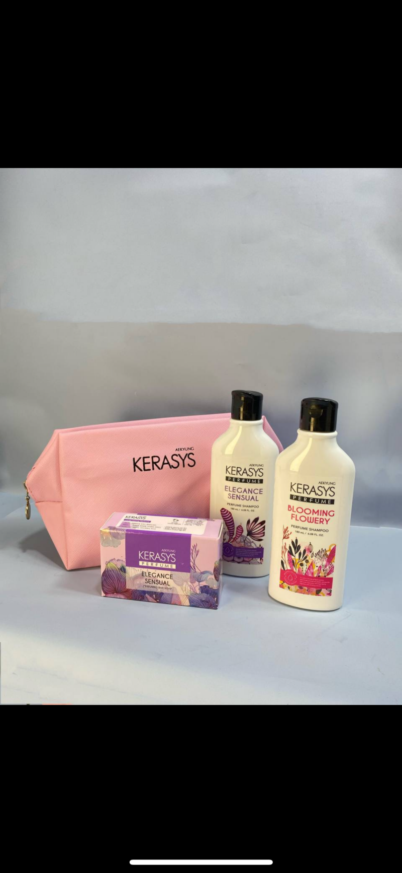 A pink cosmetic bag and a set of Kerasys hair products are arranged on a light surface, featuring a box of Elegance Sensual soap, and bottles of Elegance Sensual and Blooming Flowery perfume shampoo.