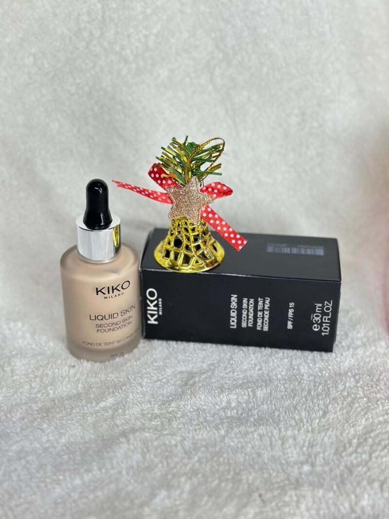 A bottle of KIKO Liquid Skin Second Skin Foundation stands next to its packaging, with a decorative golden bell with a star and a red polka-dot bow on top.