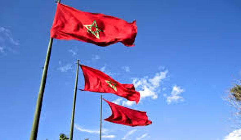 Three red flags with a green star in the center fly against a bright blue sky with scattered clouds.