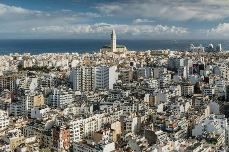 An aerial shot of a densely packed city, featuring a tall mosque or cathedral in the background near the sea.