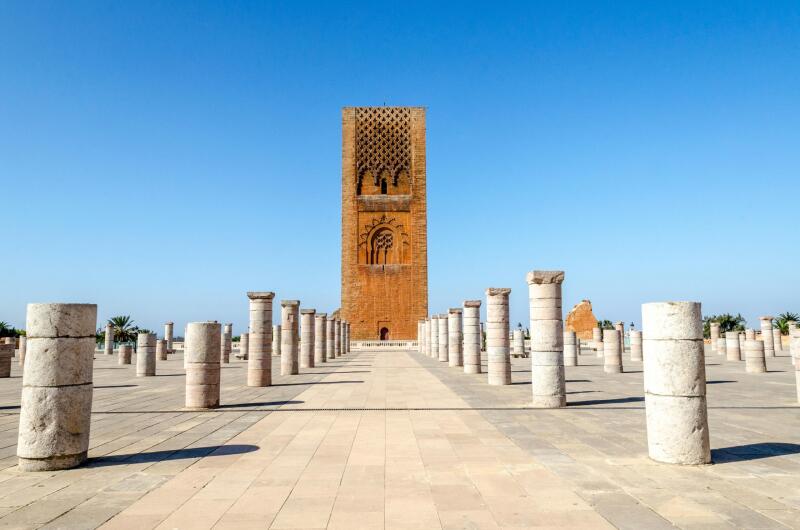 The Hassan Tower in Rabat, Morocco, is surrounded by numerous pillars on a paved ground under a clear blue sky.