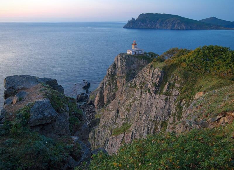 The image shows a lighthouse on a cliff overlooking the sea with an island in the background.