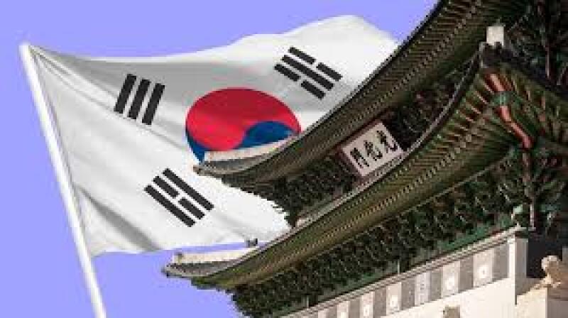 The image shows the flag of South Korea waving in front of a traditional Korean building with intricate roof details and signage.