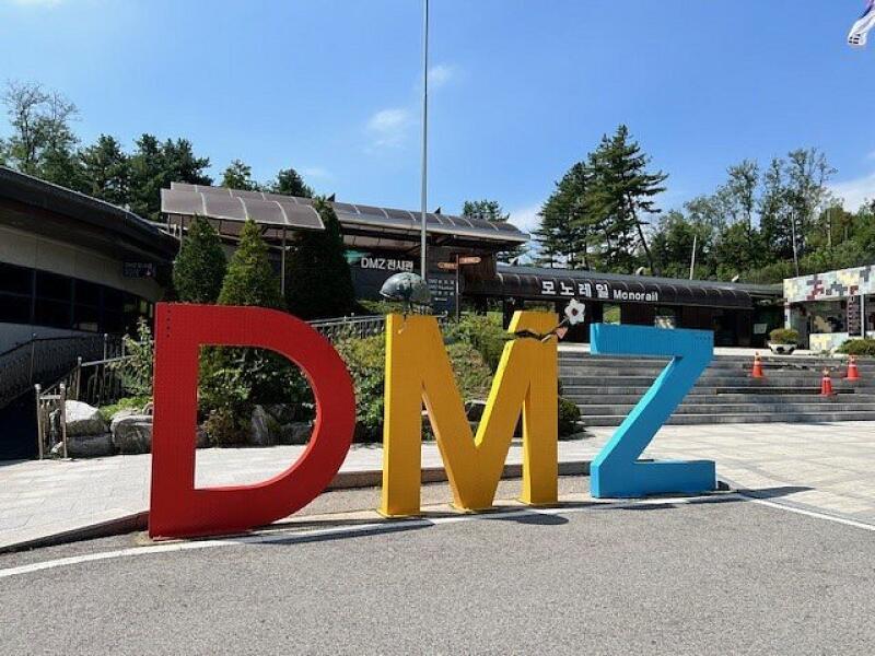 A large, colorful "DMZ" sign stands in front of a building with the text "모노레일 Monorail" on it.