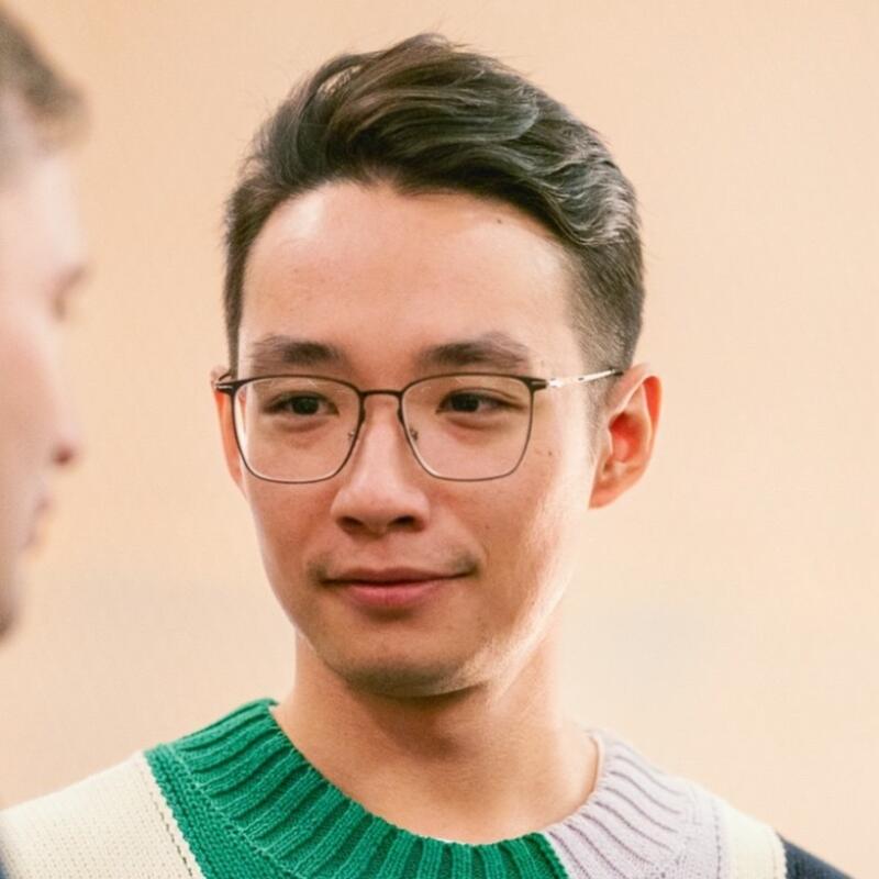 A man with dark hair and glasses wears a striped sweater.