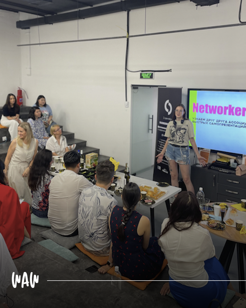 Женщина стоит перед группой людей, представляя презентацию о нетворкинге, при этом на экране за ней видно слово "Networker".