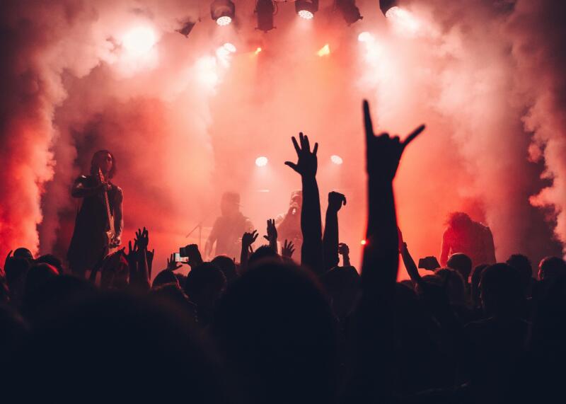 A crowd of people is silhouetted in front of a stage with red lighting and smoke.