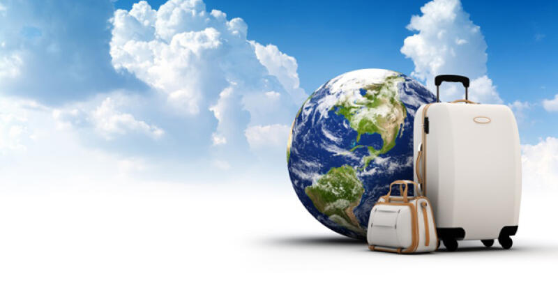 A globe is positioned next to two white suitcases against a backdrop of blue sky and clouds.