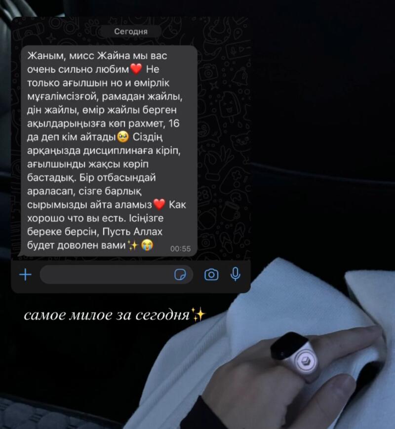 A screenshot of a message with text in Russian and Kazakh. The text expresses appreciation and affection towards a person named Zhaina. The message includes words of gratitude for her teachings and blessings. In the bottom right corner of the photo, there is a hand wearing a ring.