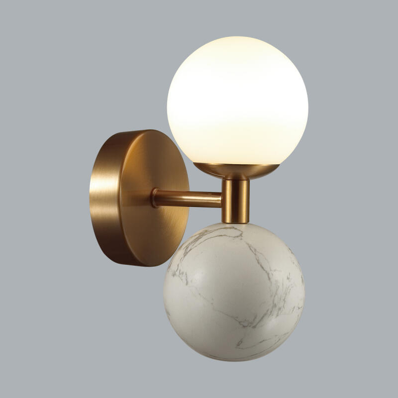 A wall lamp features a gold-colored base with a white, glowing spherical bulb on top and a white marble-patterned spherical bulb on the bottom.