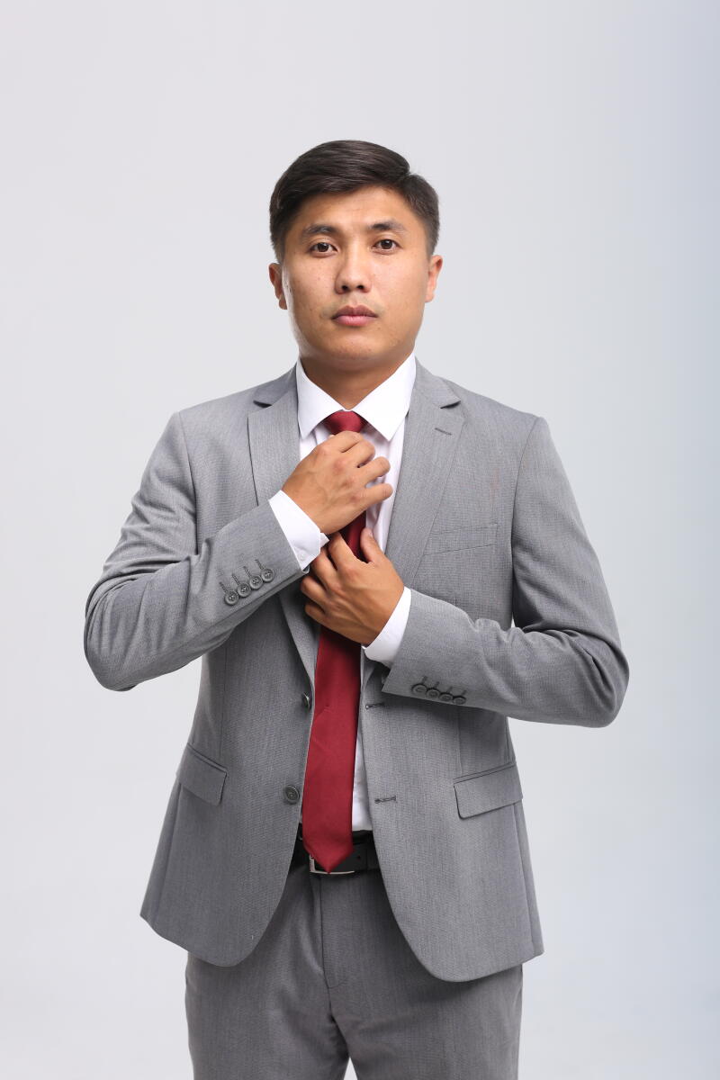 A man in a gray suit and white shirt is adjusting a red tie.