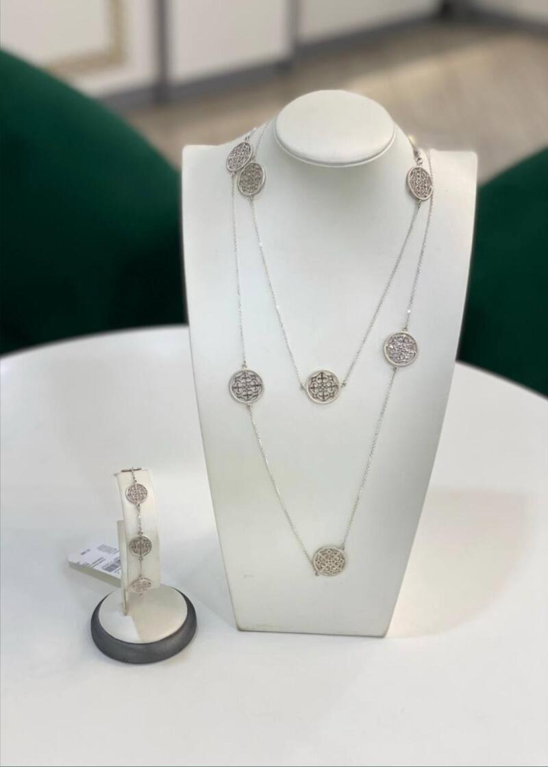 A silver necklace and bracelet with circular pendants are displayed on white stands.