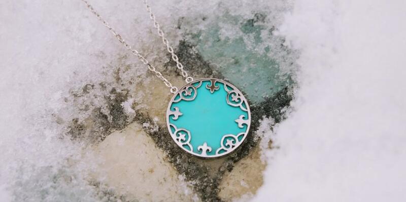 A silver necklace with a round turquoise pendant lies on a snowy surface.